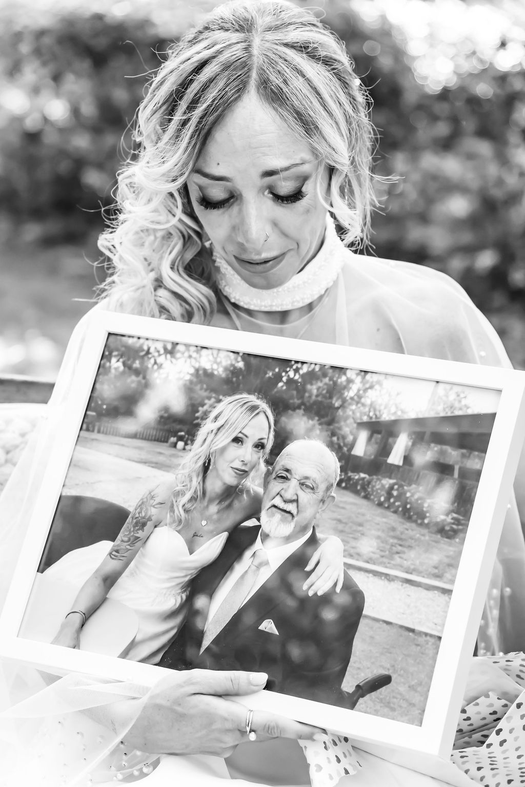Novia emocionada sosteniendo una fotografía familiar durante la ceremonia, en blanco y negro