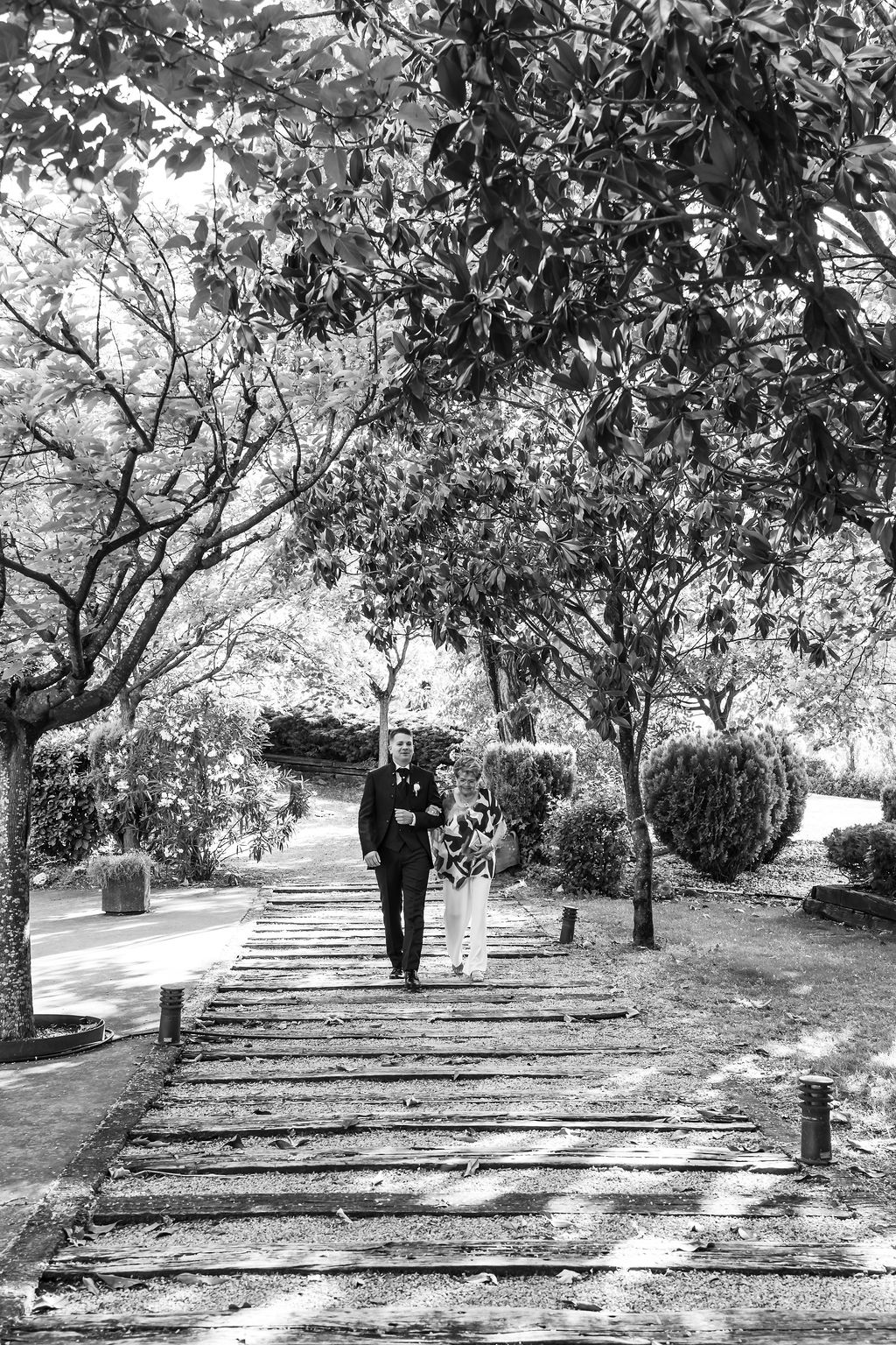 Novio caminando hacia la ceremonia por un sendero arbolado, en blanco y negro