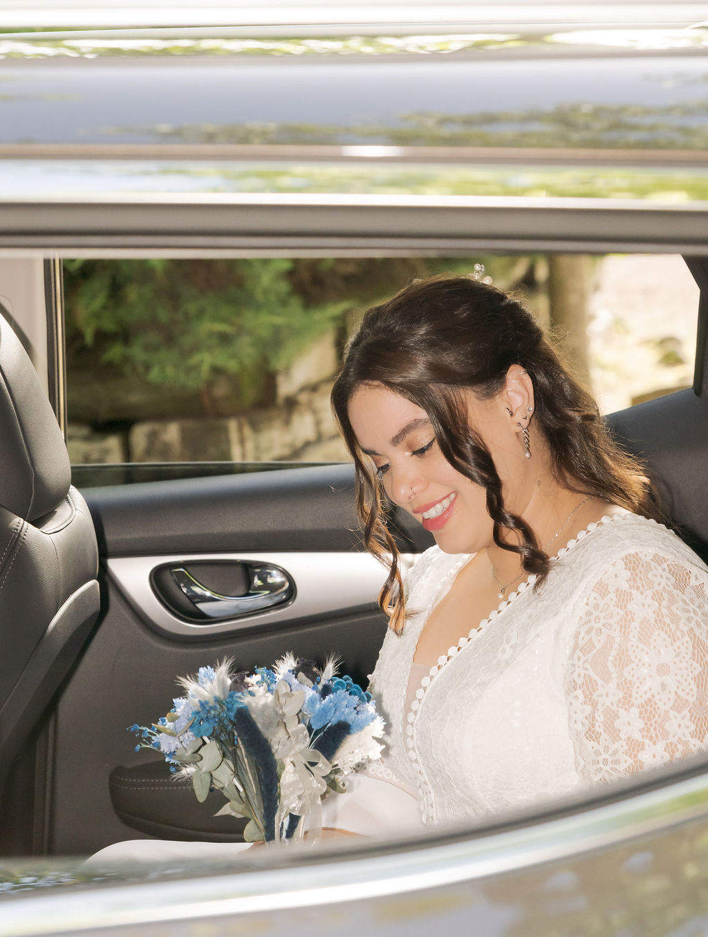 Novia sonriendo dentro del coche nupcial con su ramo antes de la ceremonia