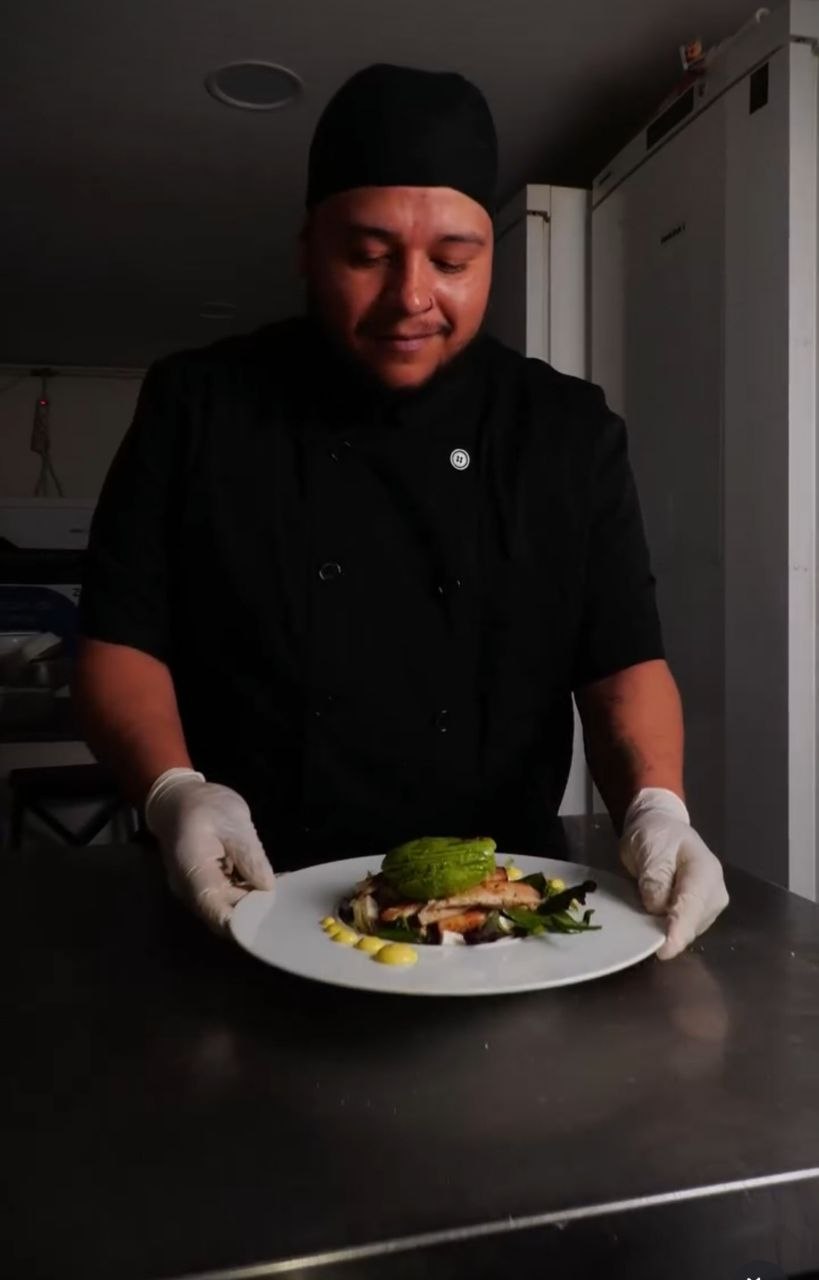 Chef presentando un plato de salmón con aguacate en la cocina de un restaurante