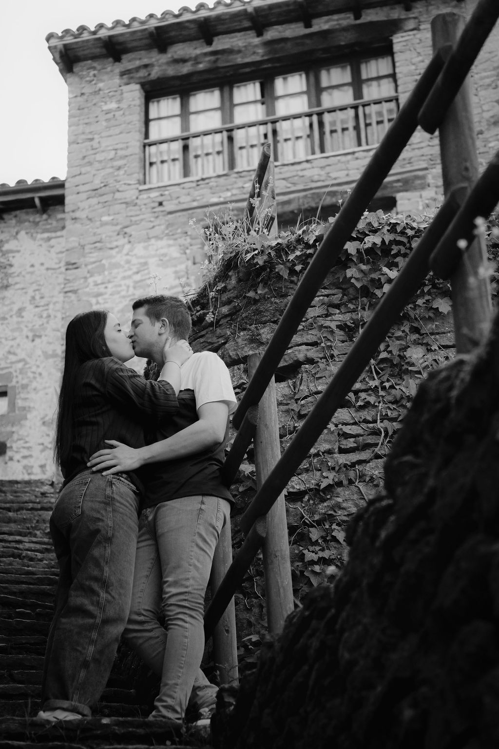 Pareja besándose en unas escaleras de piedra de un pueblo medieval, fotografía de preboda en blanco y negro